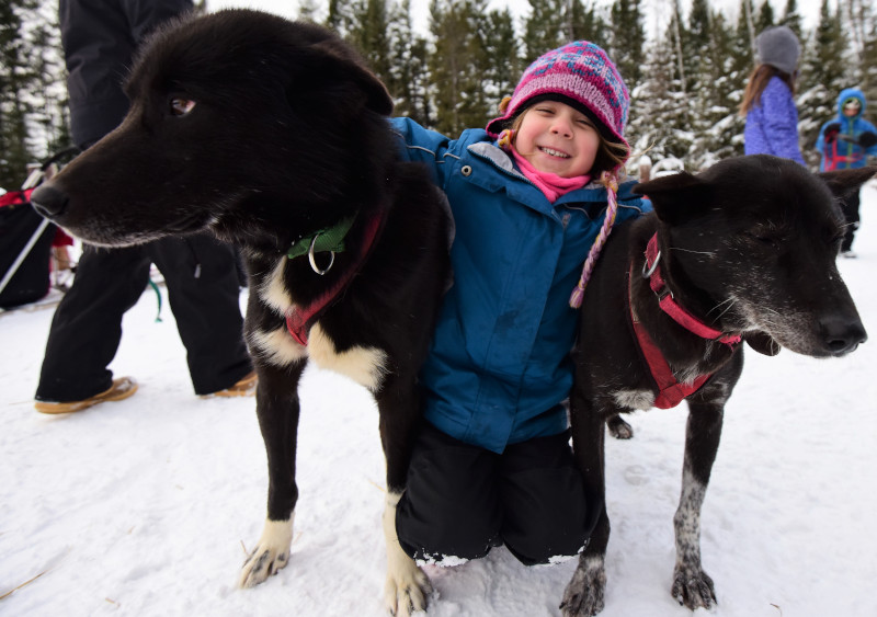 young riders embracing White Wilderness sled dogs